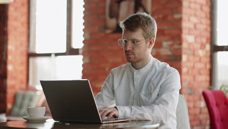 attractive-young-man-is-working-with-laptop-in-cafe-freelancer-and-independent-journalist-typing-text-on-keyboard